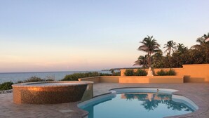 Una piscina con solárium empedrado, un jacuzzi y vista al mar.