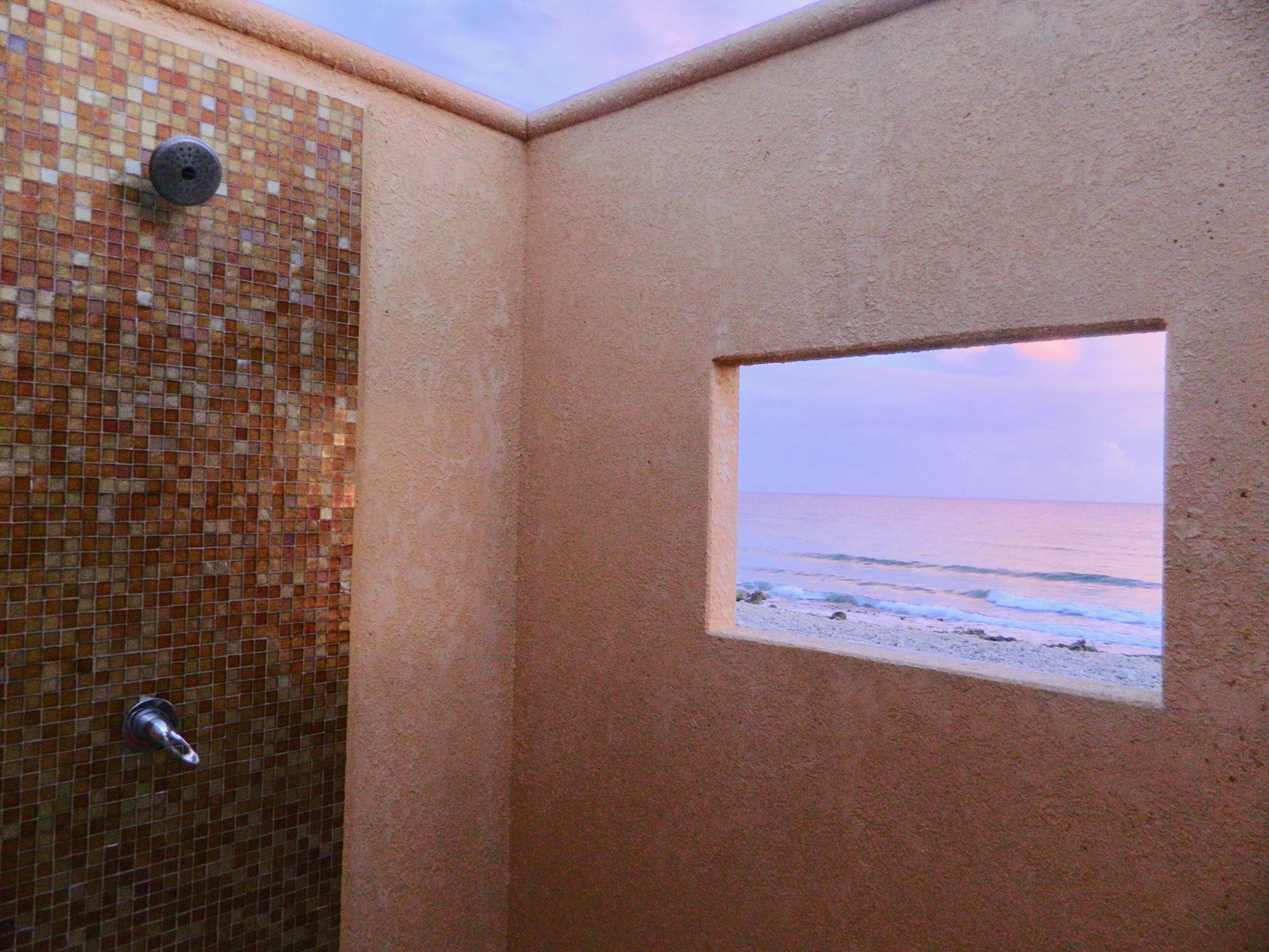 Ein Badezimmer mit Wand aus Mosaikfliesen, einer Dusche und einem Fenster mit Blick zum Strand.