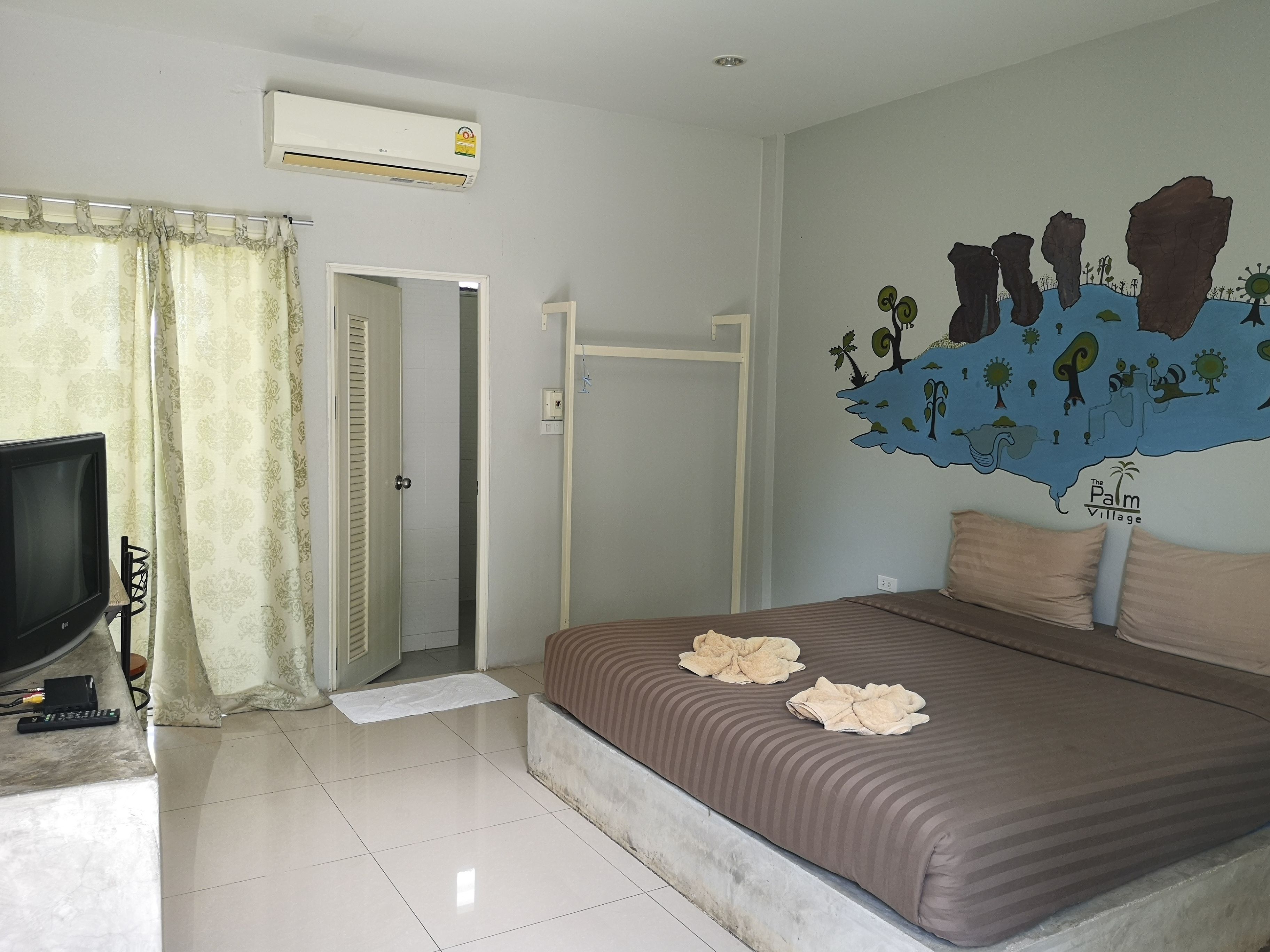 A bedroom with a bed, a TV, a door, and a wall mural.
