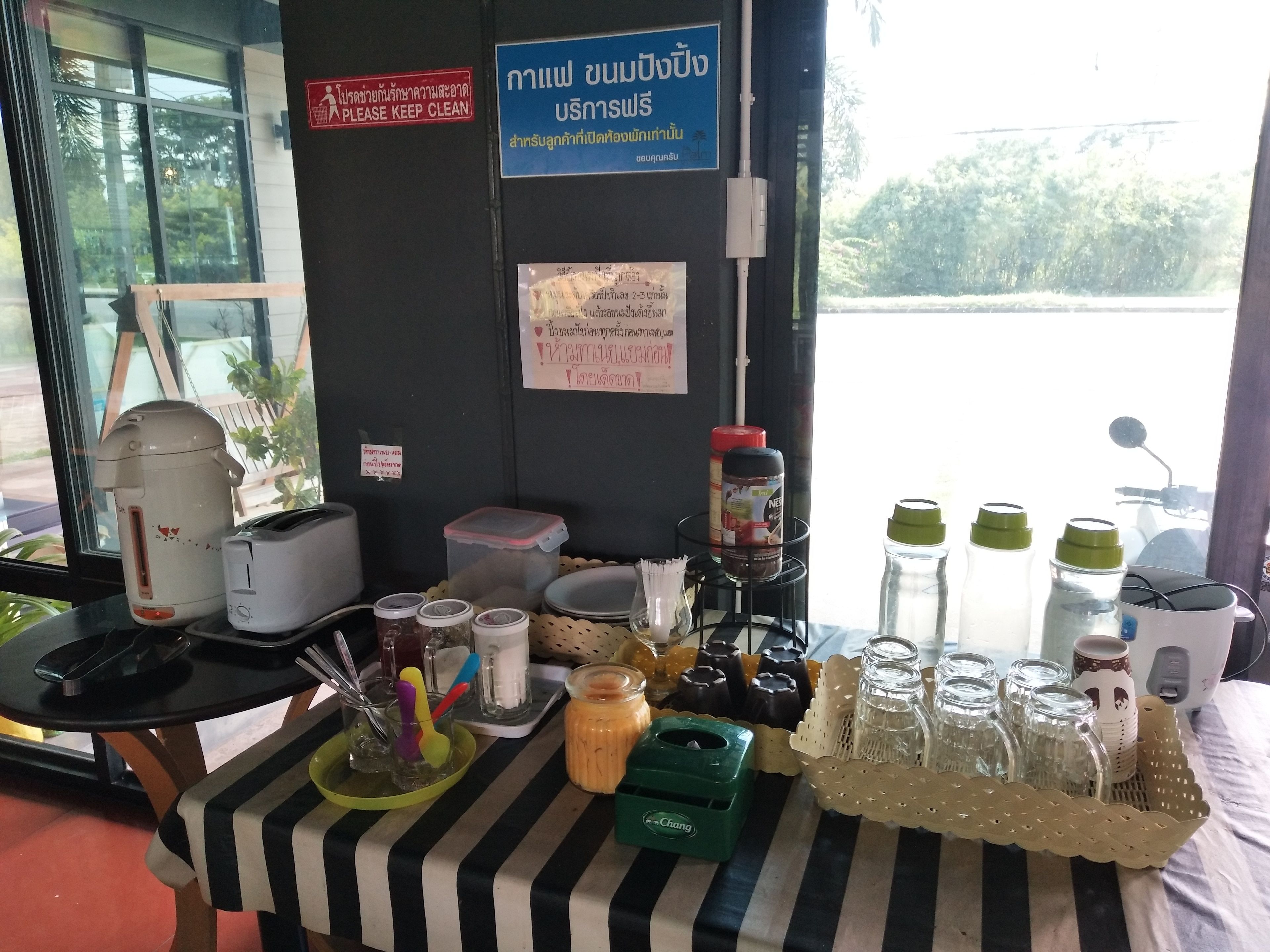 Una mesa con varios objetos, incluyendo una cocedora de arroz, frascos y botellas de condimentos, y letreros en un idioma extranjero en la pared.