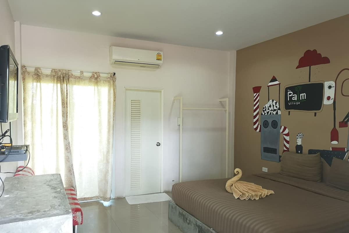 A hotel room with a bed, a desk with a computer, an air conditioner, a door, and a wall with a sign.