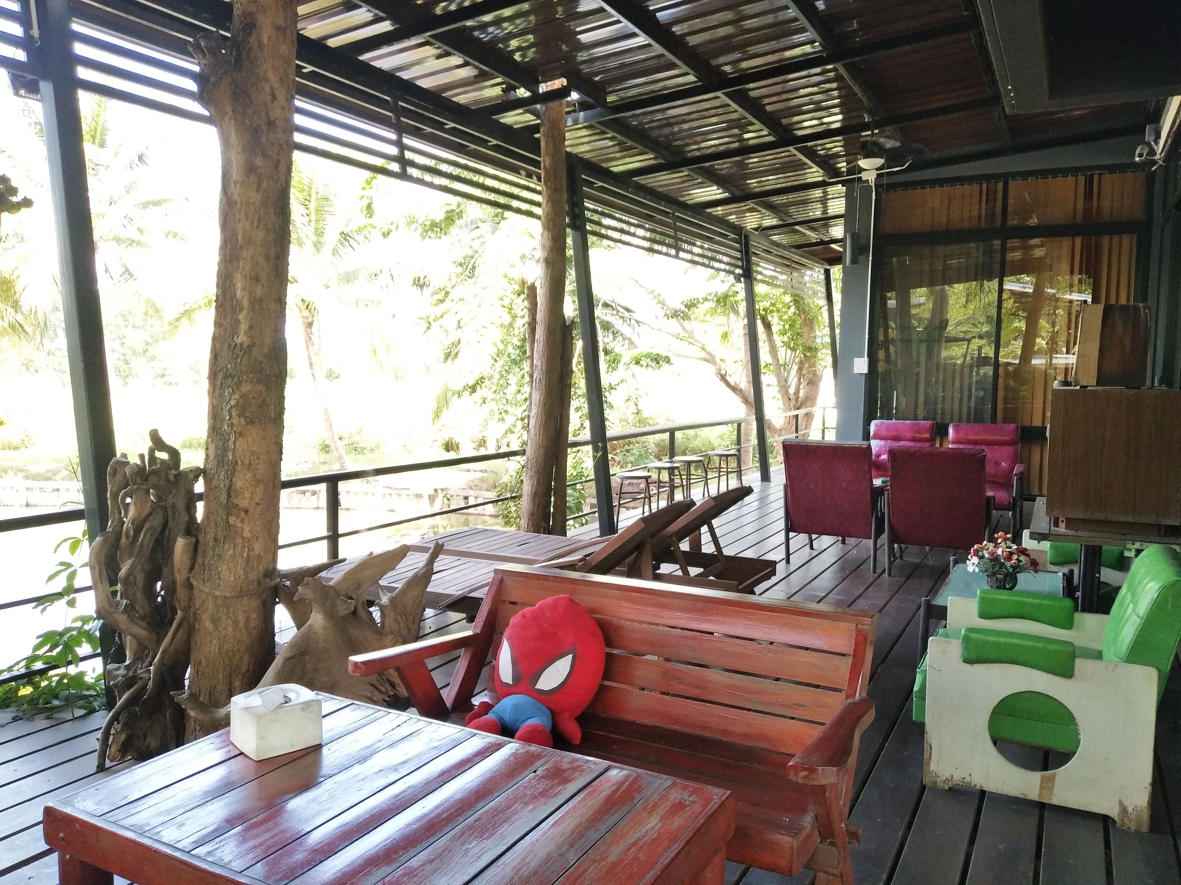 A covered outdoor seating area with wooden tables and benches, a Spiderman plush toy, and a view of the surrounding greenery.