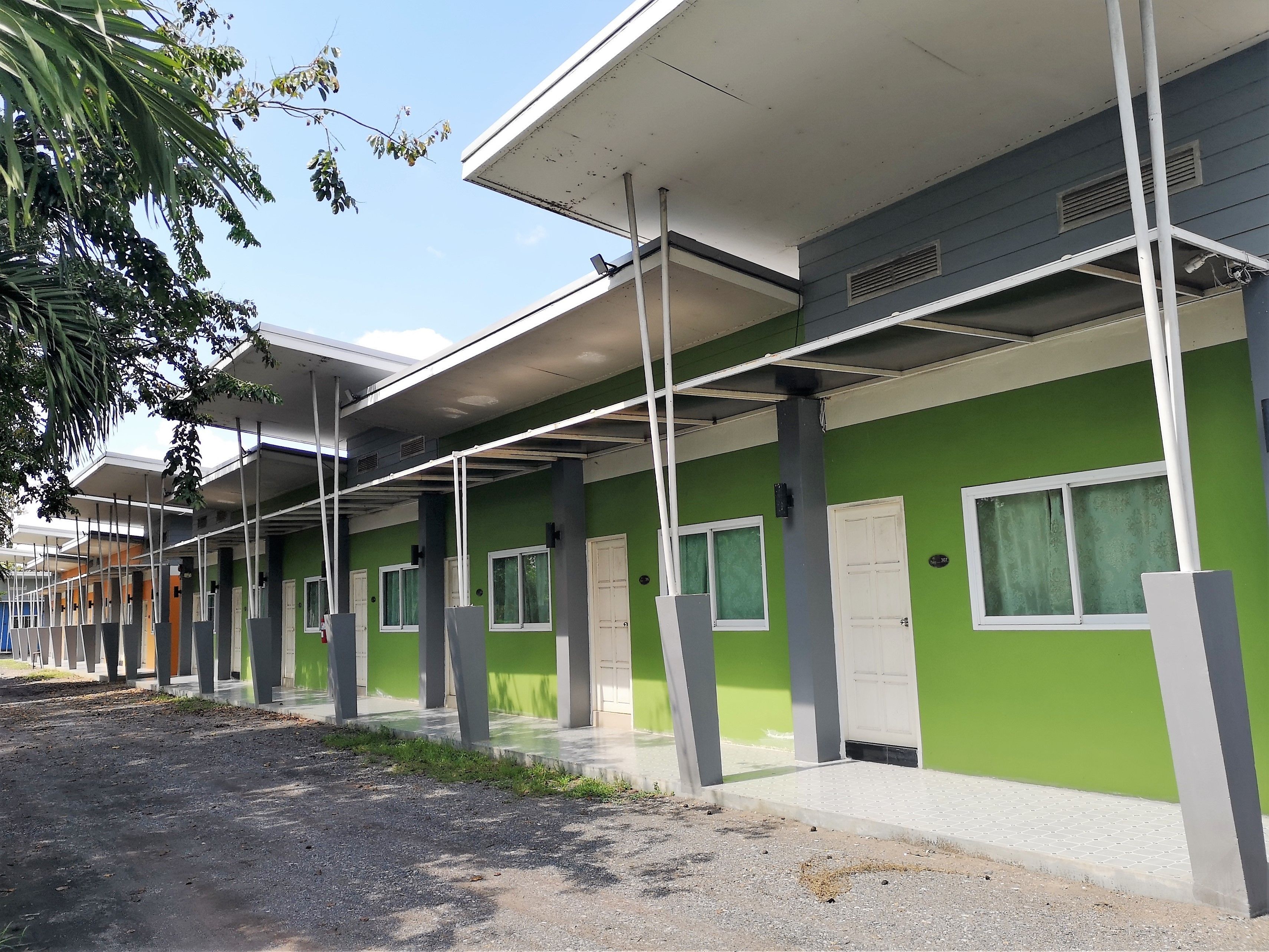 Fila de habitaciones de hotel individuales, cada una con ventana y puerta, un área exterior cubierta y una pared verde.