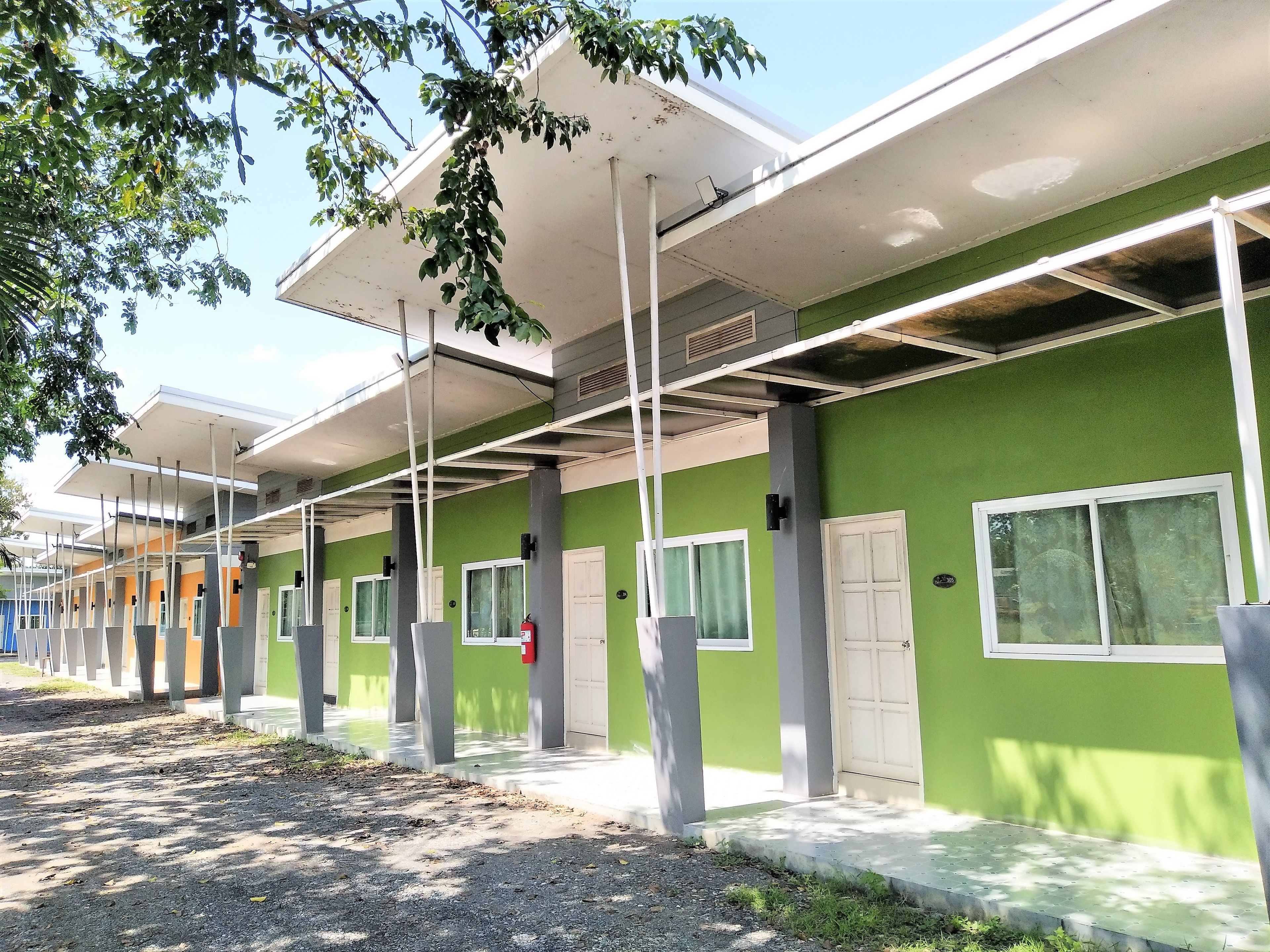 A row of green buildings with white doors and windows, supported by grey pillars, under a covered walkway.