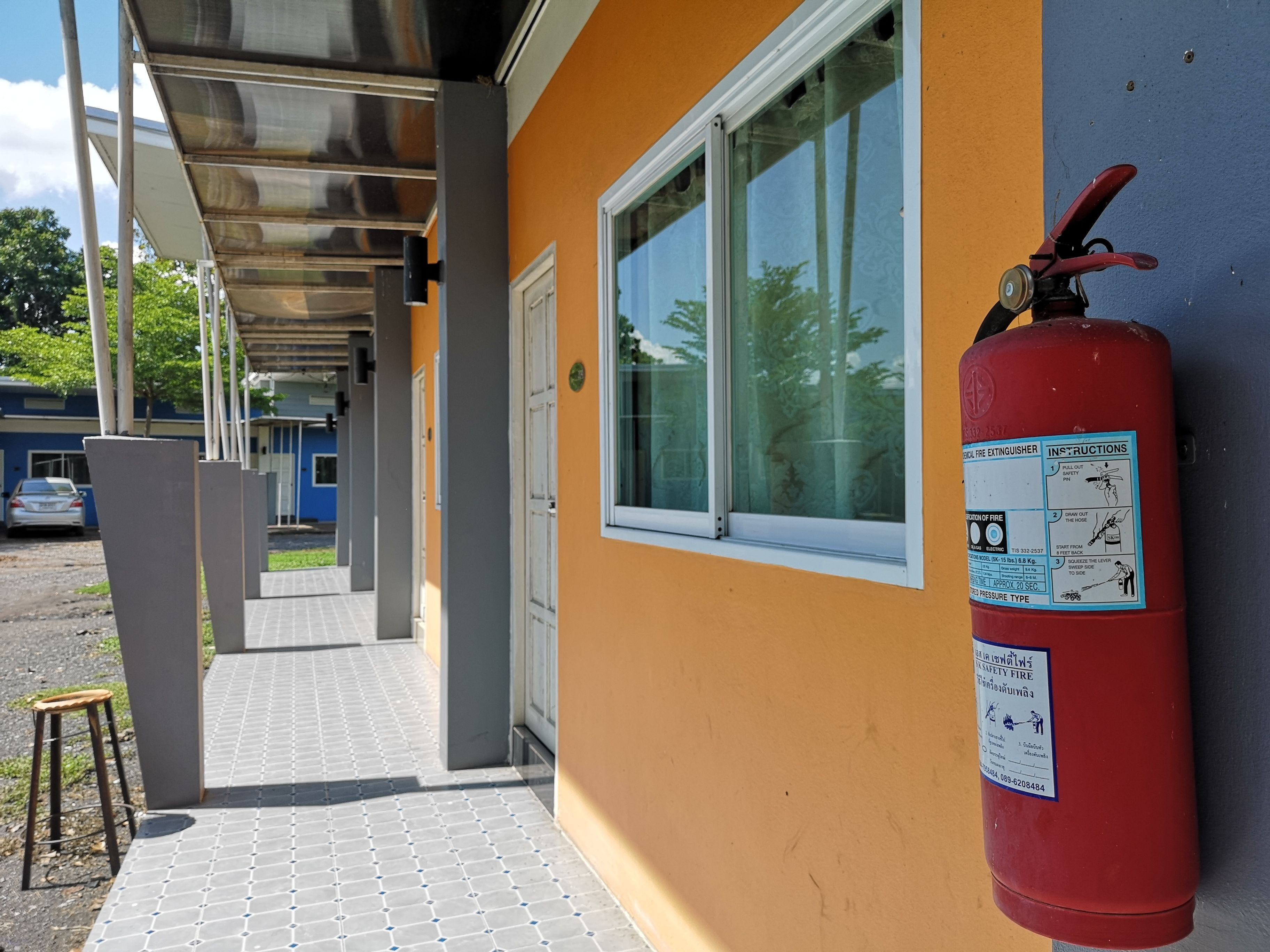 Ein an der Gebäudewand befestigter Feuerlöscher, ein überdachter Gang und eine Tür zu einem Innenraum.
