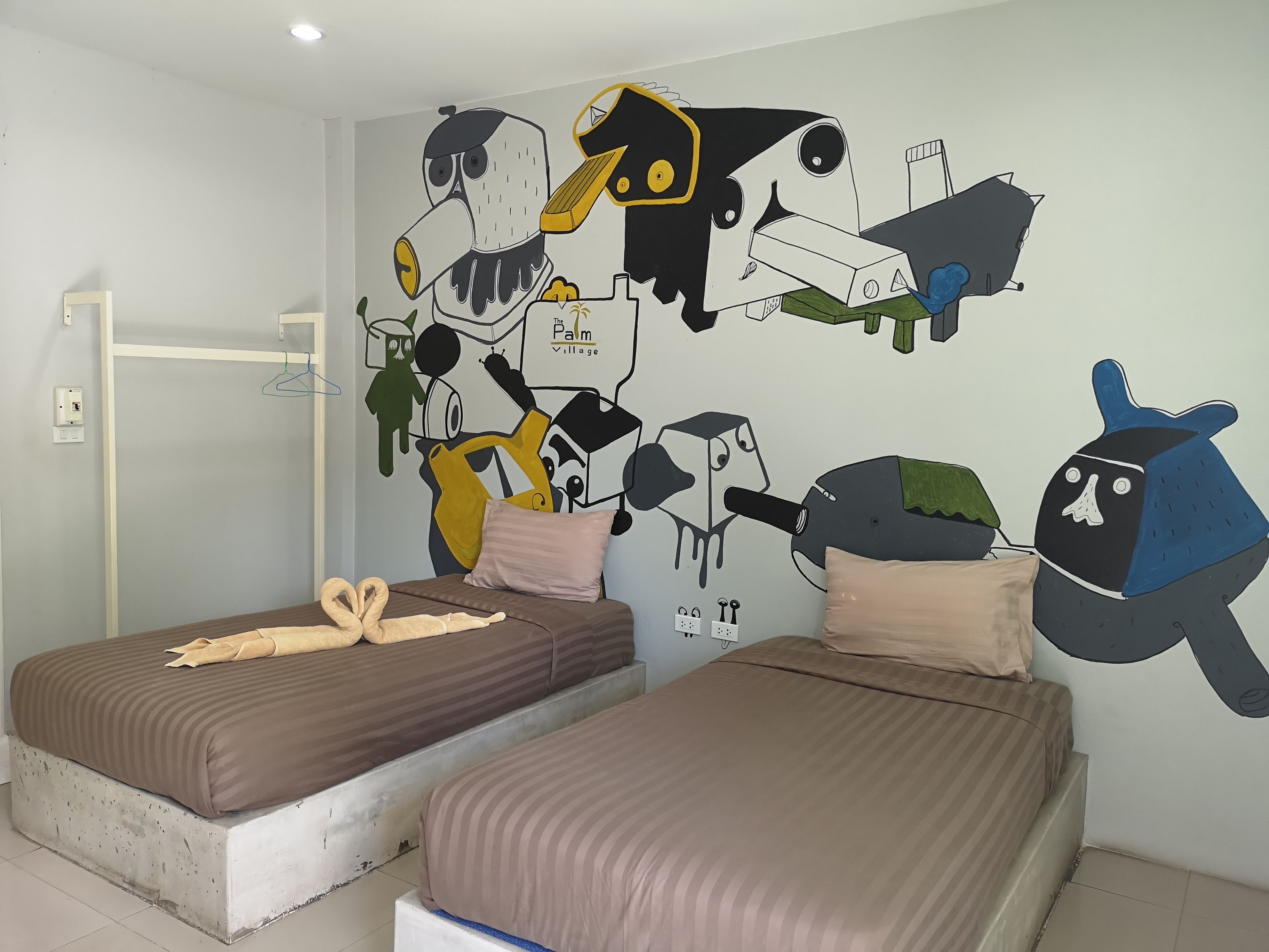 Quarto com duas camas, um mural na parede e um cabideiro.