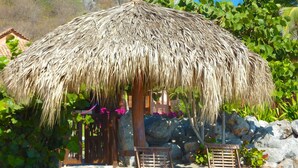 A thatched-roof hut with two wooden lounge chairs in front.