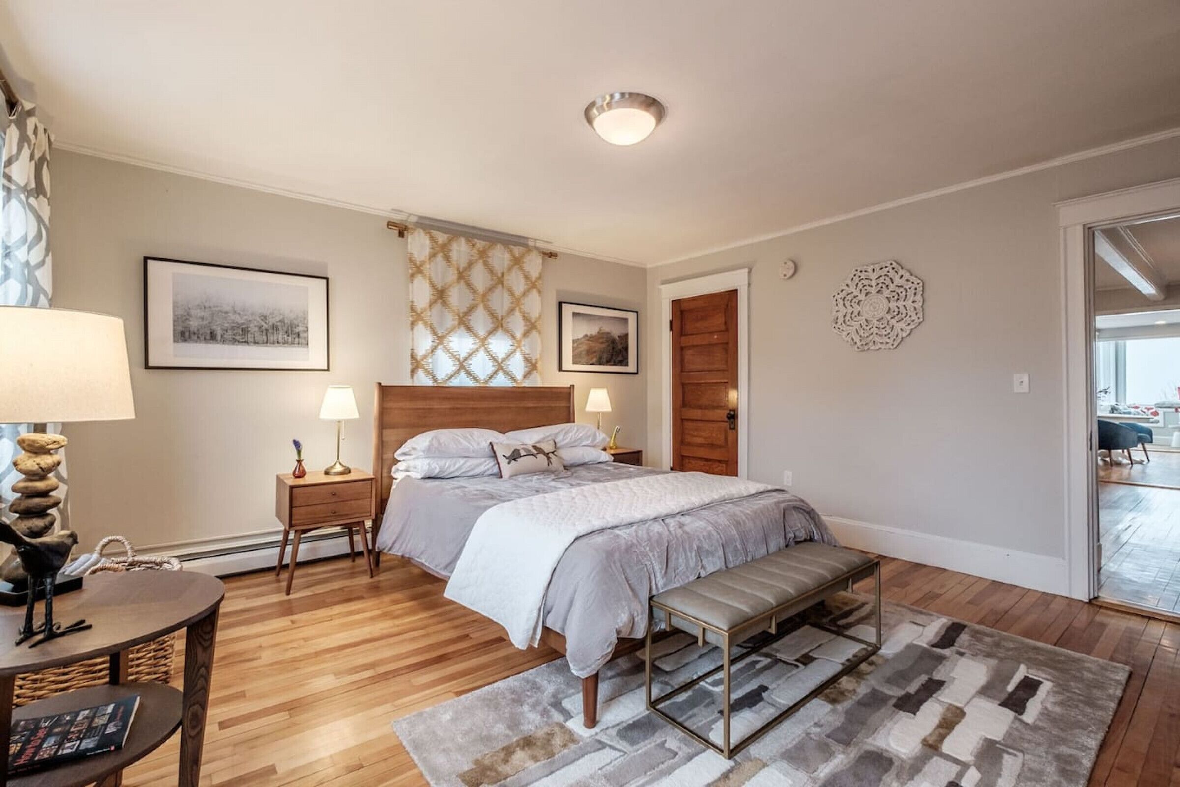 A bedroom with a bed, bedside tables, a bench, a rug, and a wooden floor.