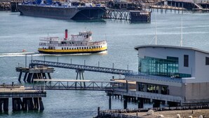A ferry boat on a river, a bridge, and a modern building with large windows.