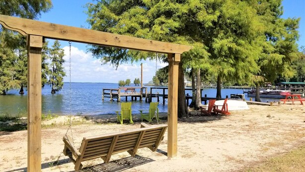 A wooden swing set and bench by a lake with a dock and boats in the background.