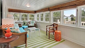A sunroom with a striped floor, wicker furniture, and large windows. - Spacious Isle of Palms Beach House with Private Pool, One Block To The Beach (Isle of Palms)