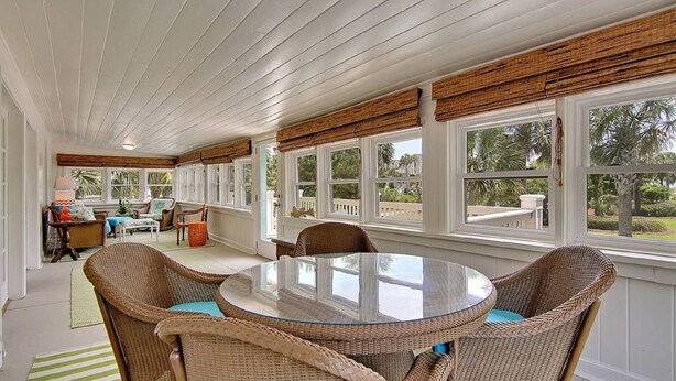 A covered patio with wicker furniture, large windows, and a view of the outdoors. - Spacious Isle of Palms Beach House with Private Pool, One Block To The Beach (Isle of Palms)
