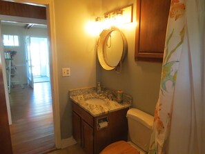 Une salle de bain équipée de toilettes, d’un lavabo et d’un miroir. Il y a un rideau de douche orné d’un motif de poissons.