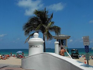 Une plage avec un poste de surveillance pour les sauveteurs, un panneau interdisant la consommation de boissons alcoolisées et un palmier.