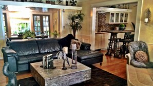 A living room with a dark leather sofa, a wooden coffee table, and a bookshelf. There is a kitchen area visible in the background. - VOTED BEST FORT LAUDERDALE LOCATION! WALK TO SHOPS, RESTURAUNTS, & BEACH. (Ft Lauderdale)