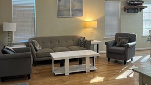 A living room with a sofa, armchair, coffee table, and a ship model on a shelf.