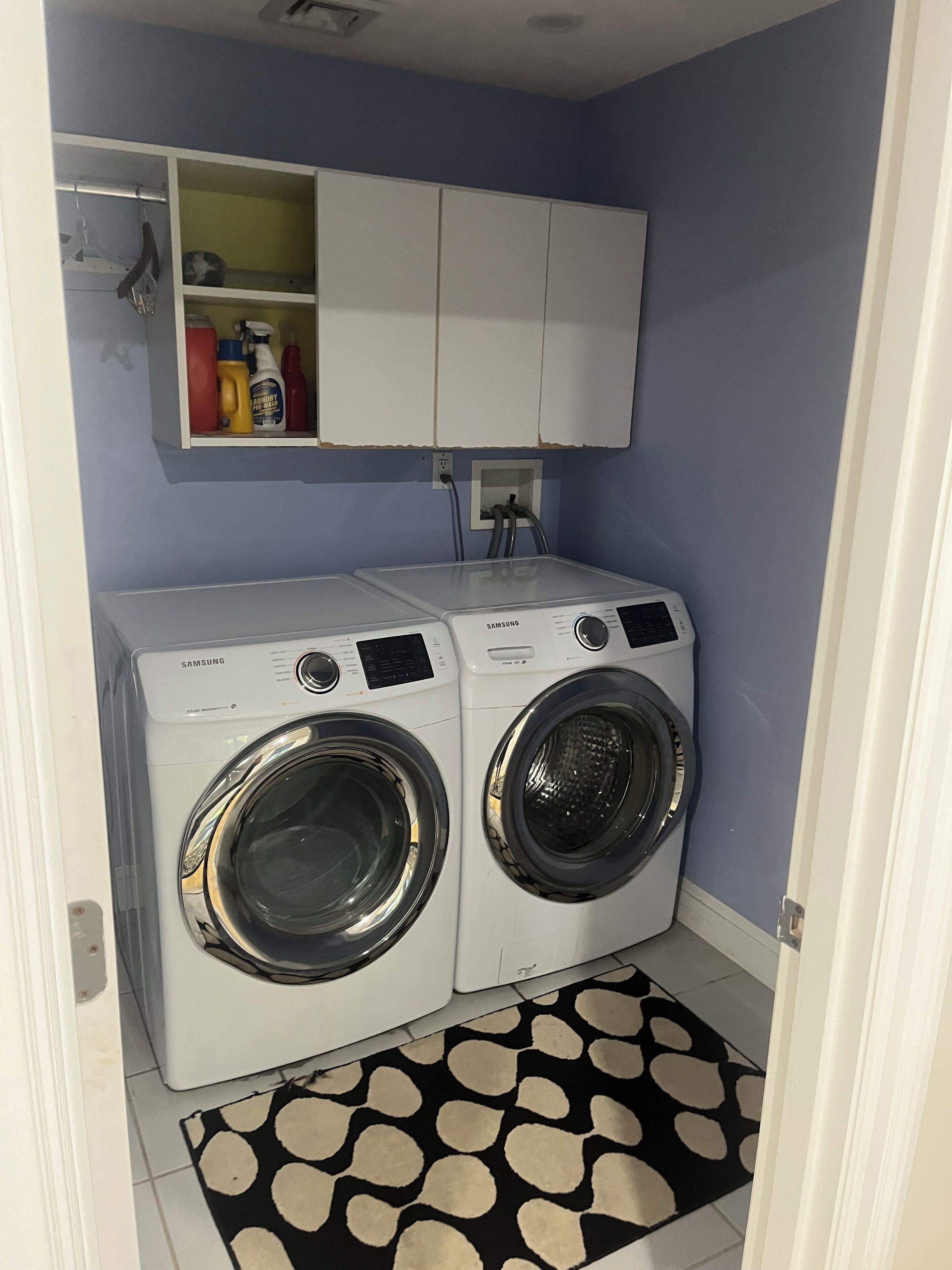 Een wasserij met twee Samsung wasmachines, een kast erboven en een vloerkleed met patroon.