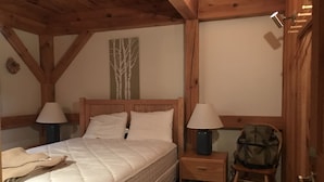 A bedroom with a wooden ceiling, a bed with white bedding, two bedside lamps, a nightstand, and a chair. - Rustic and cozy Walk In-Walk Out Ski Condo (Carrabassett Valley)