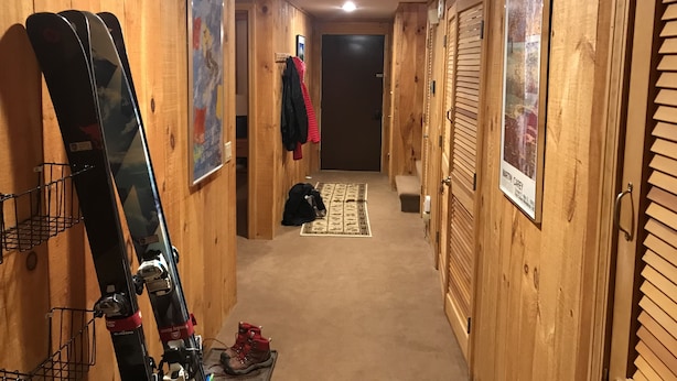 A wooden hallway with skis leaning against the wall, a coat rack with jackets, and a door at the end. - Rustic and cozy Walk In-Walk Out Ski Condo (Carrabassett Valley)