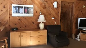 A wooden-paneled room with a black leather armchair, a wooden cabinet, a framed picture, a lamp, and a television. - Rustic and cozy Walk In-Walk Out Ski Condo (Carrabassett Valley)