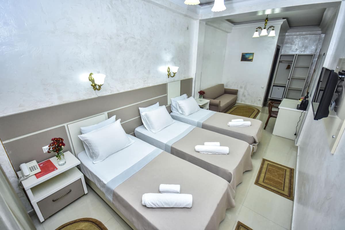 A hotel room with three beds, a small desk, a telephone, and a mirror.
