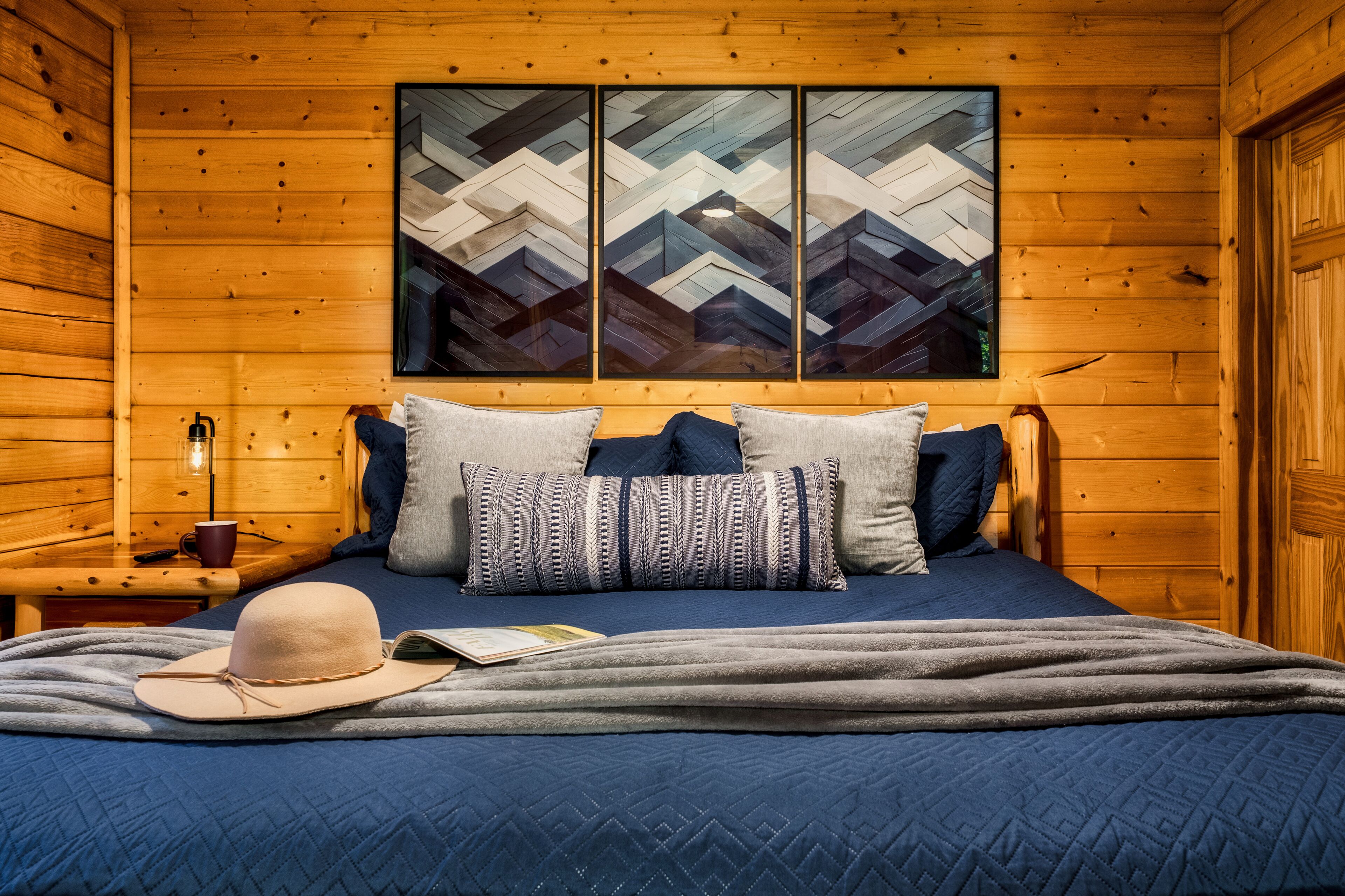 A wooden cabin room with a bed, pillows, a hat, and a book.