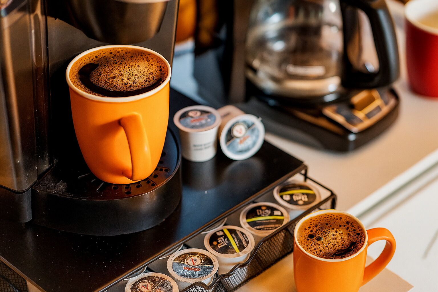 A coffee machine with two cups of coffee, a coffee pot, and a coffee maker on a kitchen counter.