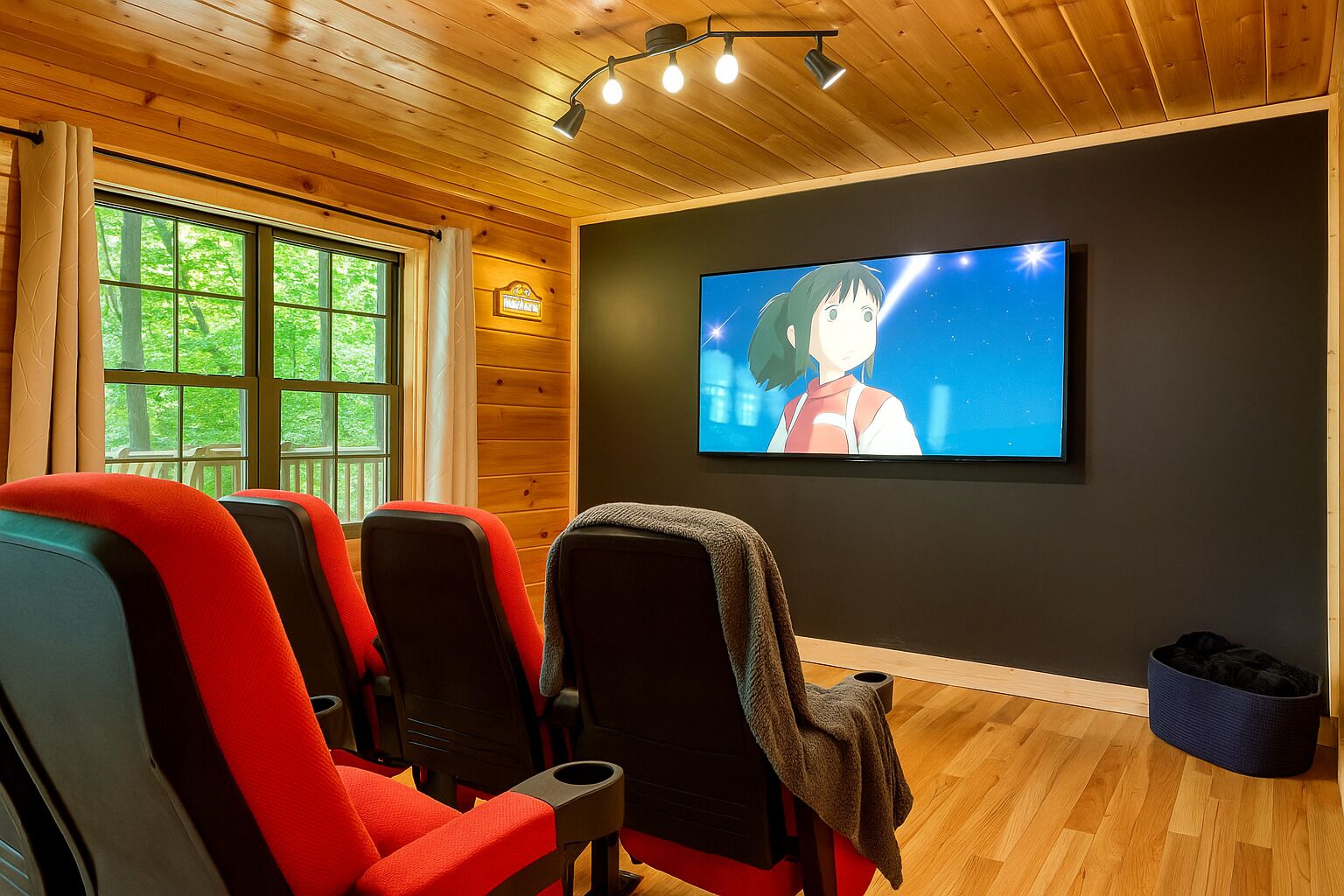 Una habitación acogedora con paredes y techo de madera, una pantalla de televisión grande y tres sillas rojas y negras.