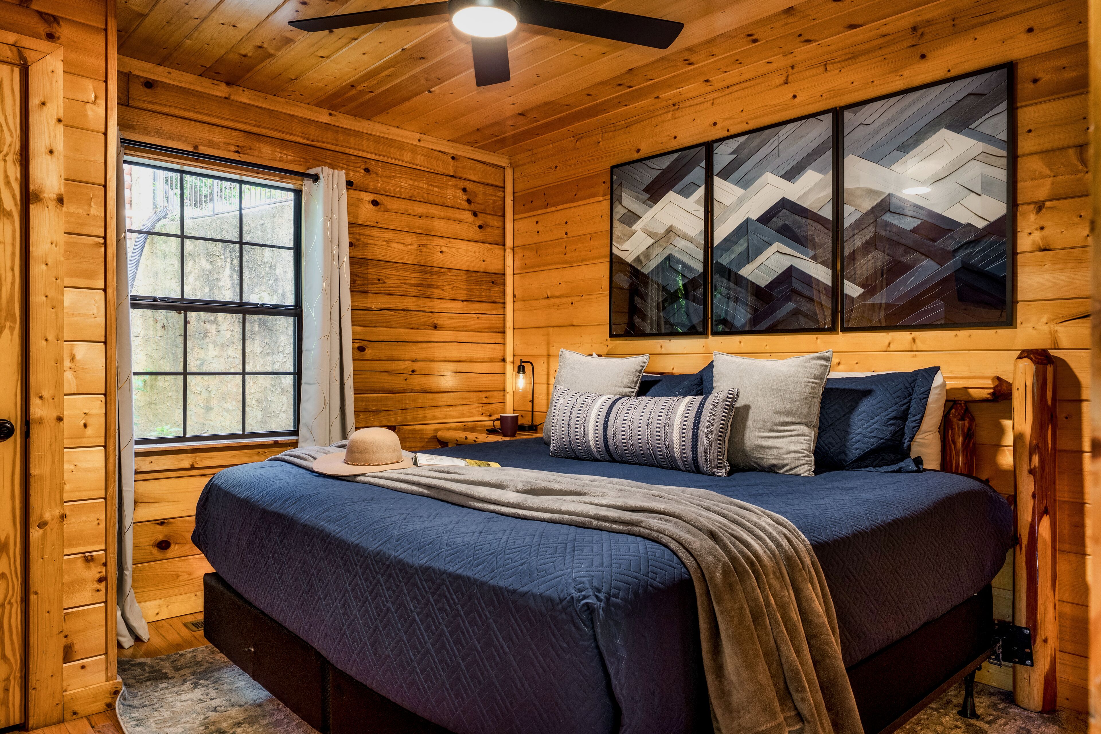 A wooden cabin bedroom with a large bed, a window, and a ceiling fan.