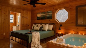 A cozy bedroom with a bed, a window, a bathtub with candles, and wooden walls.
