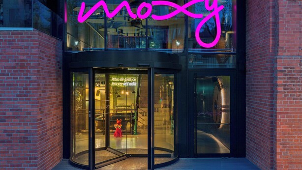 A building with a glass entrance and a neon sign spelling "mozy".