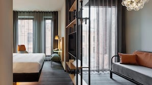 A modern hotel room with a bed, sofa, TV, and a view of the city.