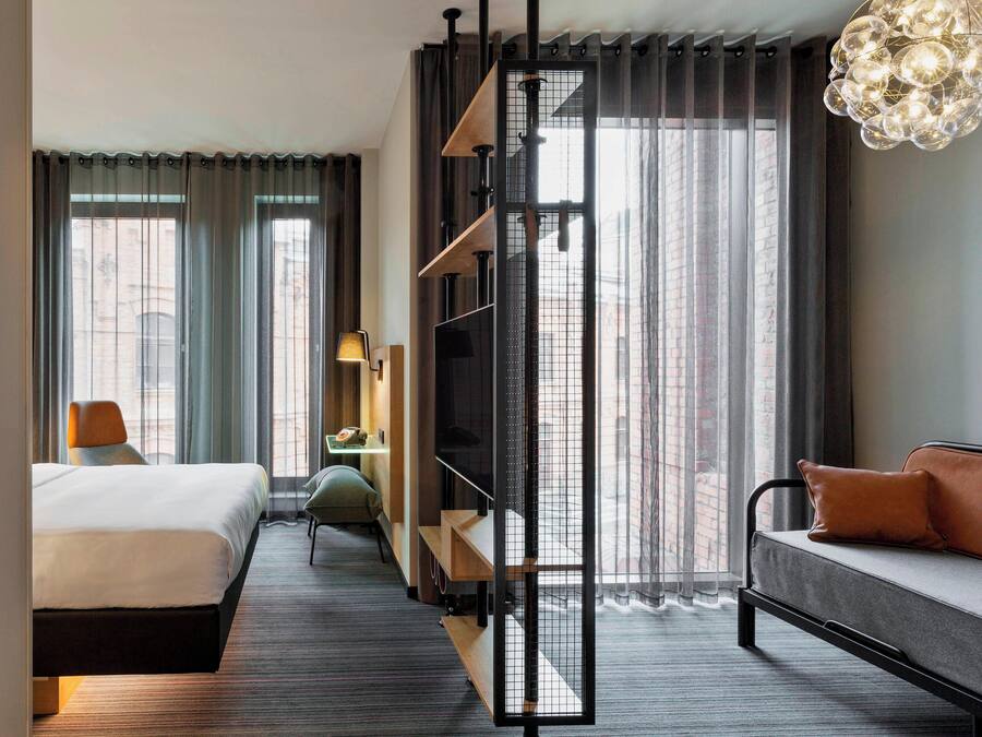 Habitación de hotel moderna con cama, sofá, televisión y vistas a la ciudad.