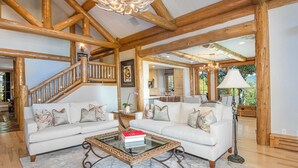 A spacious living area with a high ceiling and exposed wooden beams, a large white sofa set, a glass coffee table, and a staircase leading to another level. - Private Home with amazing views! (Avon)