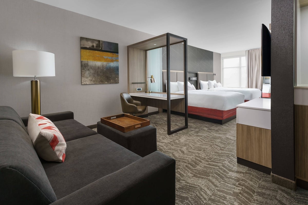 A hotel room with a sofa, a desk, a bed, and a TV.