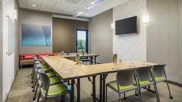 A conference room with a long table, multiple chairs, a large window, and a flat-screen TV on the wall.