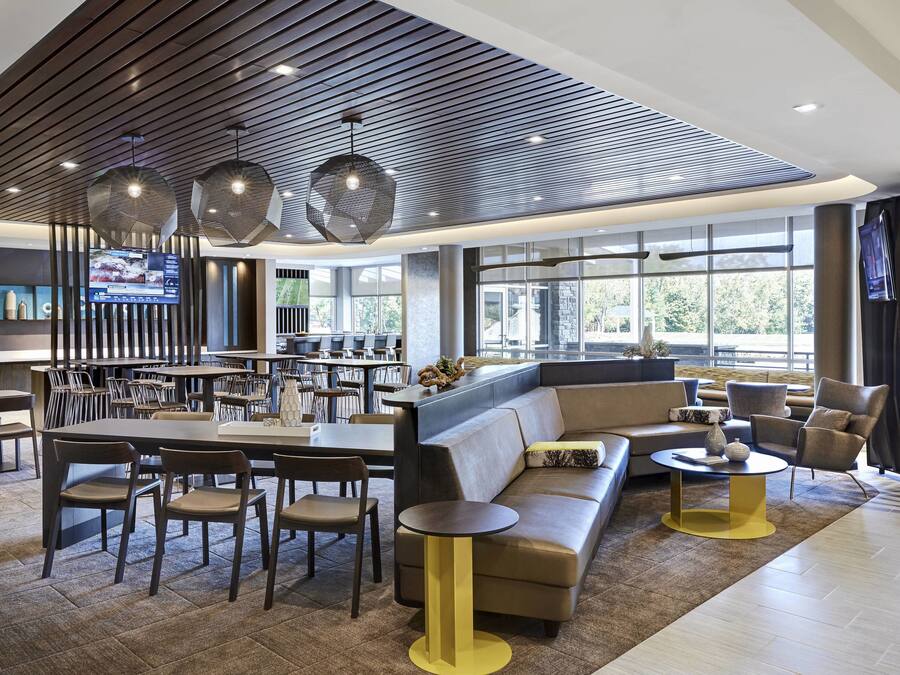 A modern hotel lobby with a bar area, seating arrangements, and large windows offering natural light.
