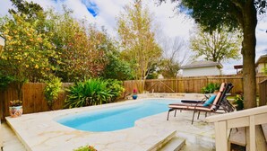 A backyard with a swimming pool, lounge chairs, and potted plants.