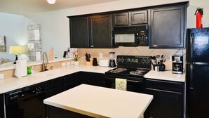 A modern kitchen with dark cabinets, a black stove, a microwave, and a refrigerator.