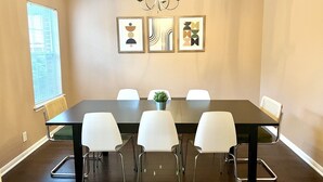 A conference room with a long table, six white chairs, a chandelier, and abstract wall art.