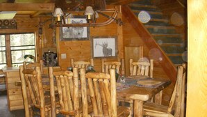 Zona d'esmorzar rústica de fusta amb taula gran i cadires, un penjoll i quadres d'animals salvatges a les parets.