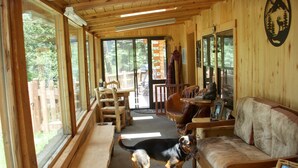 Interior d'una cabana de fusta amb un gos, mobles de fusta i una finestra gran.