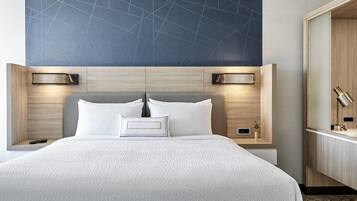 Una habitación de hotel moderna con una cama grande, dos mesitas de noche con lámparas, un velador y un armario de madera.