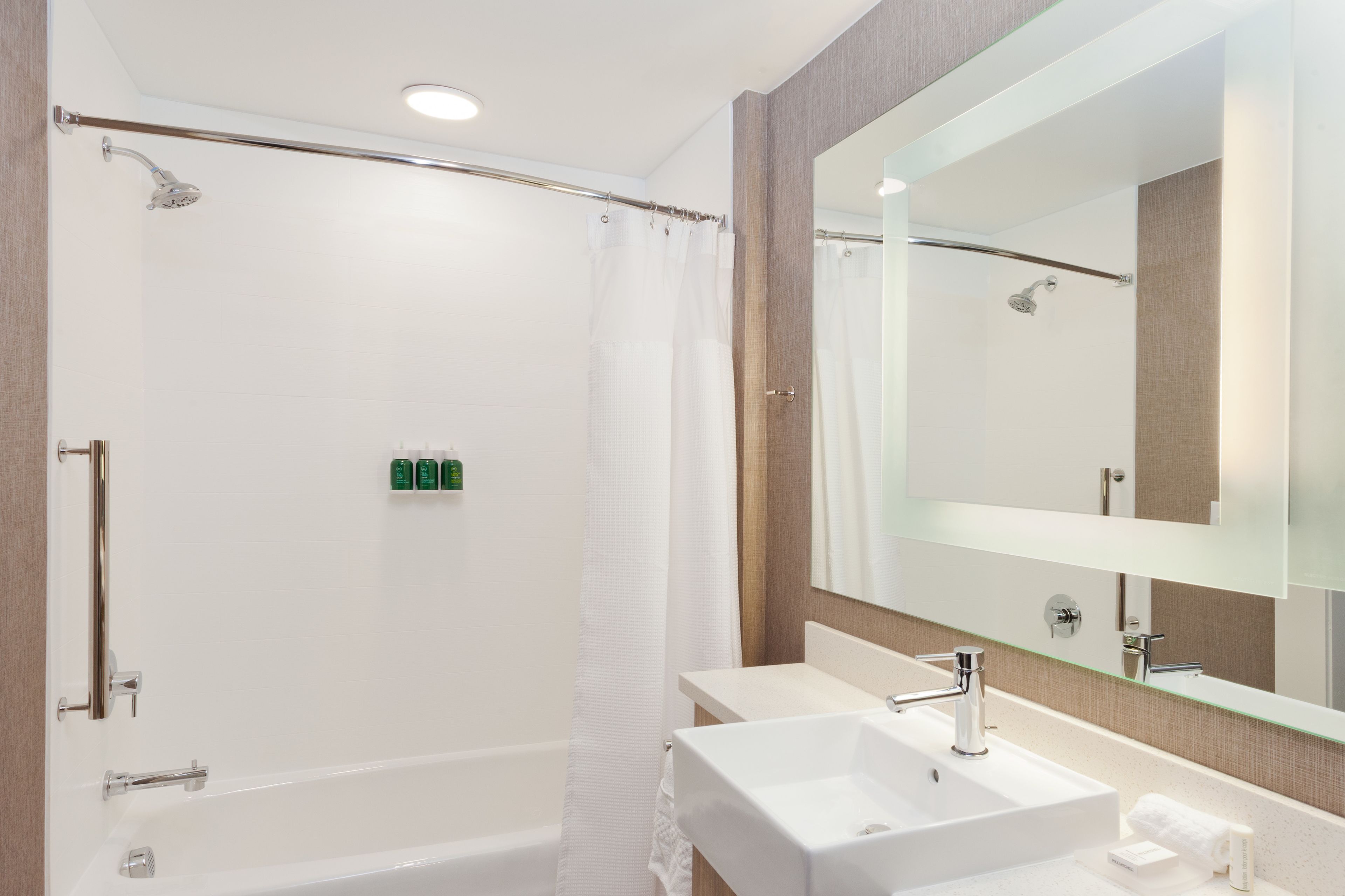 Un bany modern amb plat de dutxa, un mirall gran i un doble lavabo.