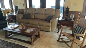 Una sala de estar con un sofá, una mesa de centro de madera, un sillón mecedora y una mesita de noche con una lámpara.