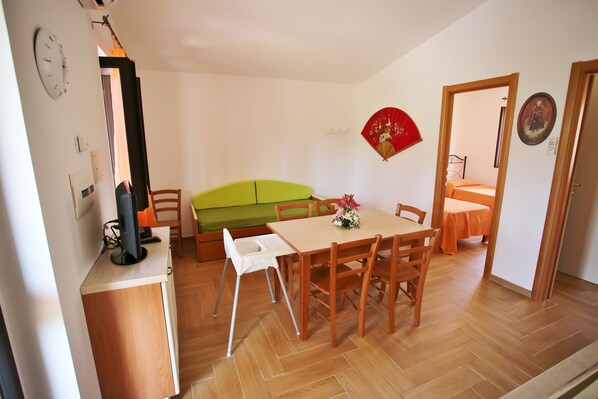 Un comedor con una mesa de madera, sillas, un sofá verde y una pequeña mesa blanca.