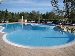 Una piscina amplia y despejada con múltiples carriles, rodeada de sillas de descanso y una terraza de piedra.