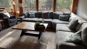 Una sala de estar acogedora con un sofá modular, una mesa de centro de madera y un ventanal con vistas a árboles.