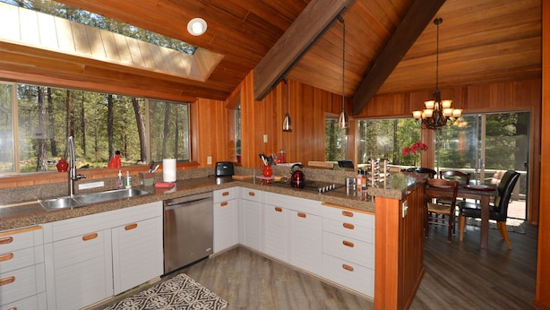 Una cocina amplia con armarios de madera, una isla grande y vistas al bosque a través de ventanas grandes.