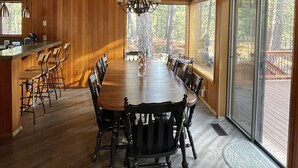 Comedor de madera con una mesa grande, sillas, una araña y ventanas amplias.